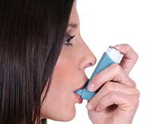Woman using an inhaler to relieve her asthma symptoms. .