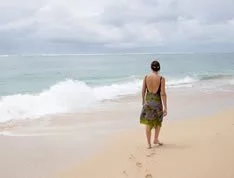 A middle aged woman walking along the shore, happy for having recovered from the disease that made her suffer