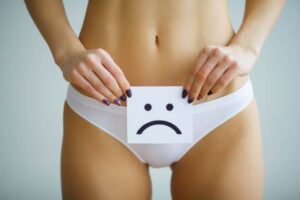 A woman in her underwear holding a sad face drawing